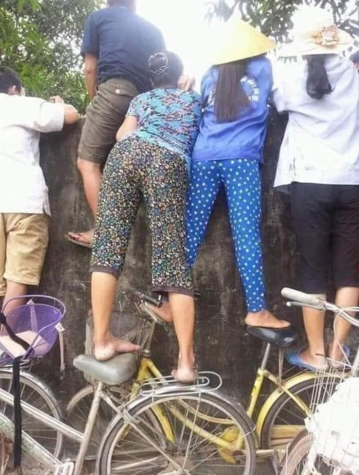 Các bà các mẹ đứng trên xe đạp nhìn qua tường hóng chuyện